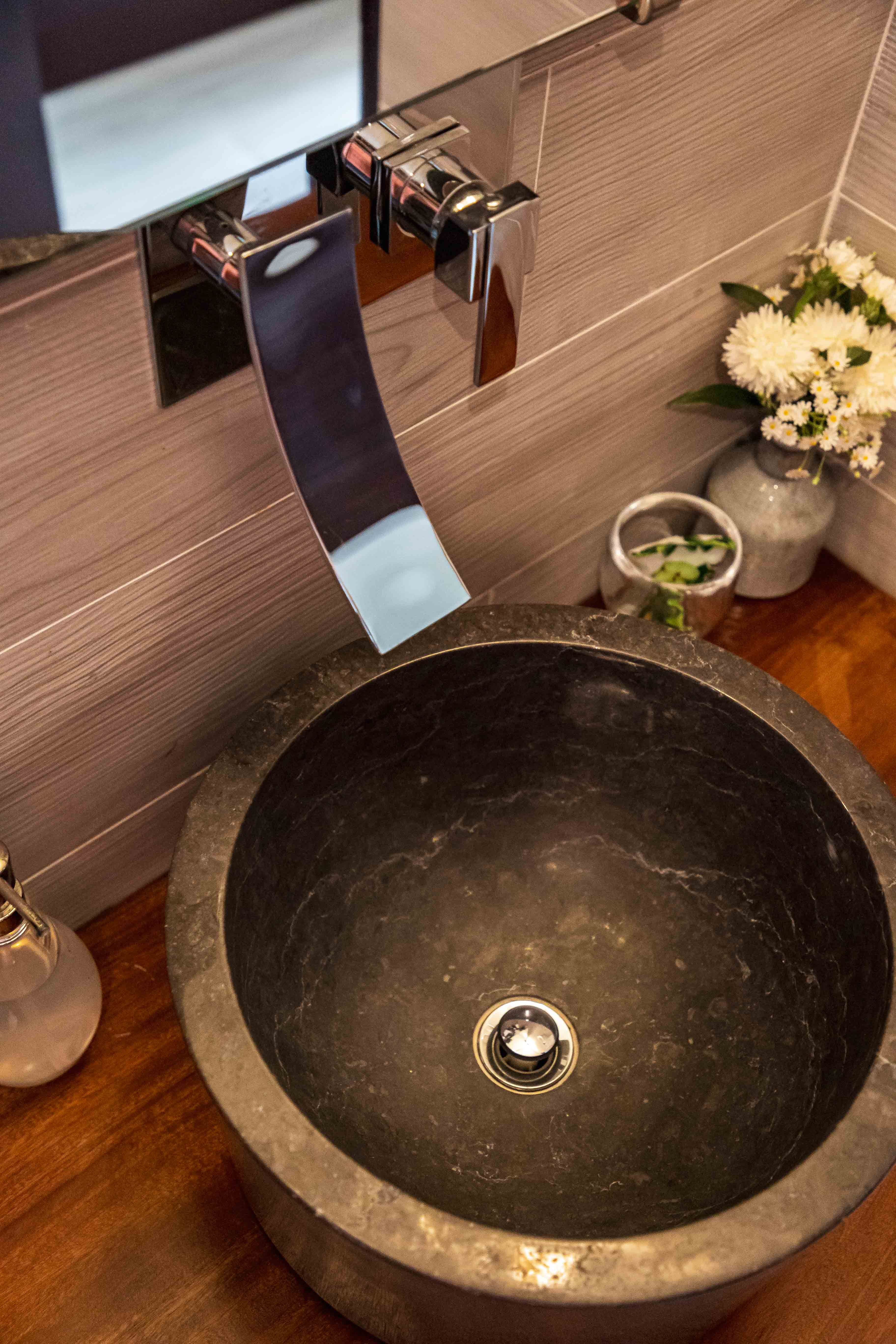 Luxury Bonaire villa spa bathroom featuring a dark natural stone vessel sink on a wood countertop with a modern wall-mounted chrome waterfall faucet.